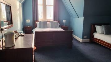 Une chambre à coucher avec un grand lit, un plus petit lit, un bureau et une fenêtre avec des rideaux.