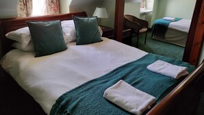 Ein Hotelzimmer mit einem großen Bett, zwei Kissen, einem Nachttisch mit Lampe, einem Sessel und einem zusätzlichen Bett in der Ecke.