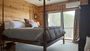 Une chambre à coucher aux murs lambrissés, dotée d’un lit à baldaquin, d’un ventilateur de plafond et d’une grande fenêtre avec des rideaux.