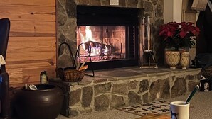Une cheminée en pierre avec un feu, un panier de bois et une tasse de café sur une table.