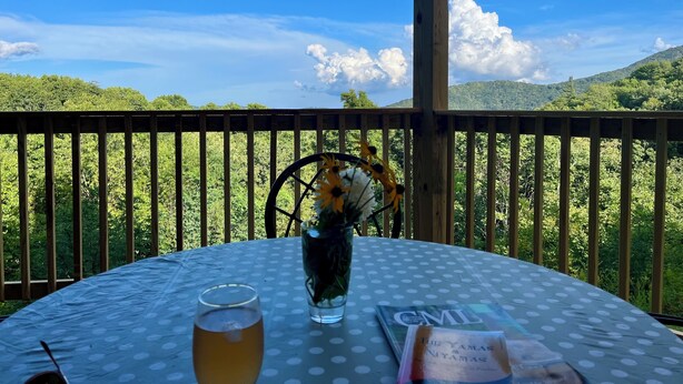 Une table ronde recouverte d’une nappe à pois, un verre contenant un liquide ambré, un vase rempli de fleurs et un livre intitulé « Les Yamas et les Nyamas ».