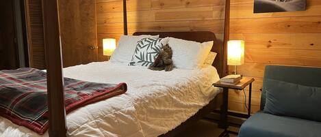A bedroom with a wooden headboard, a four-poster bed, a blue armchair, and a wall-mounted picture.