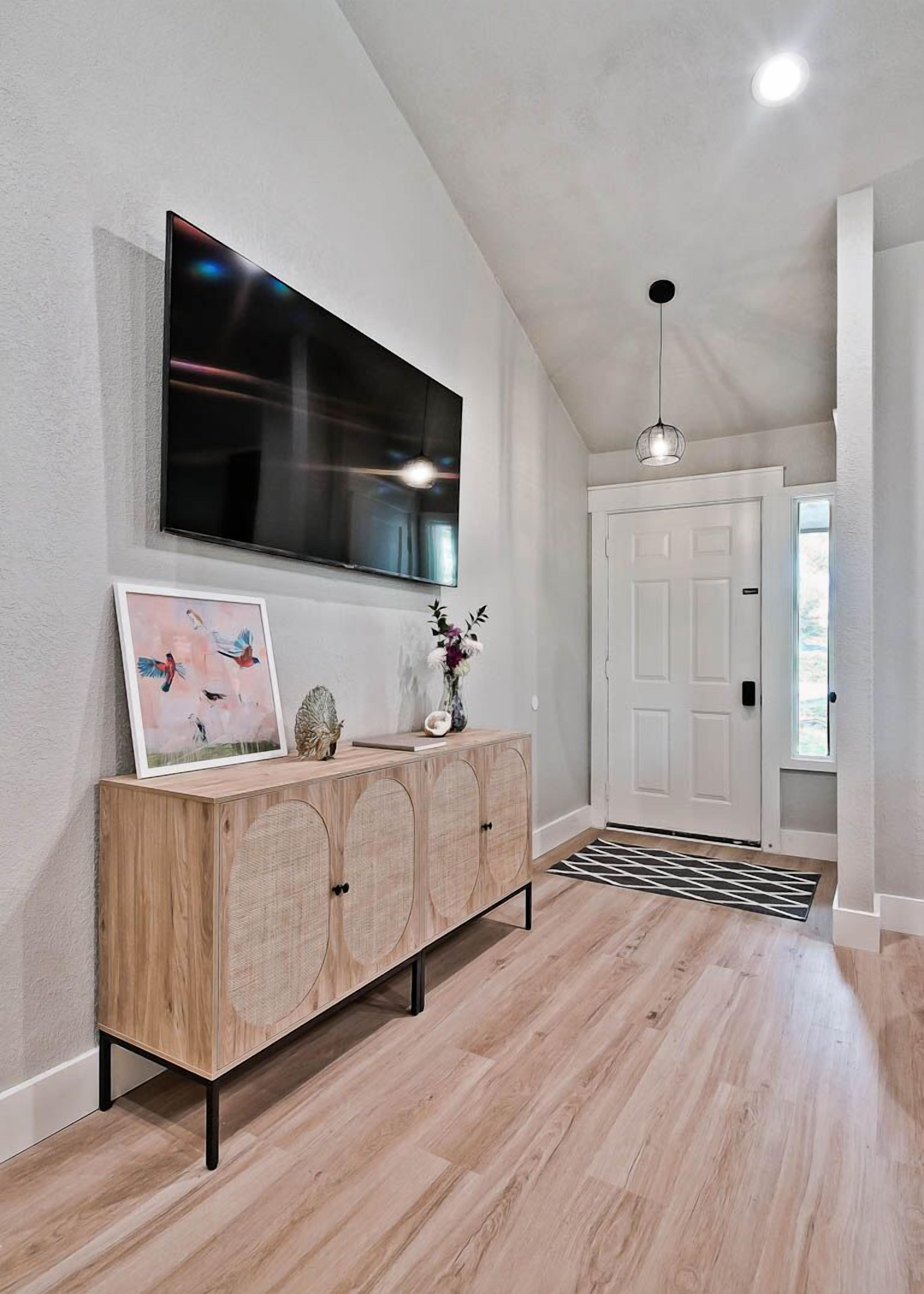 Een moderne hal met een houten console tafel, een tv aan de muur en een witte deur.