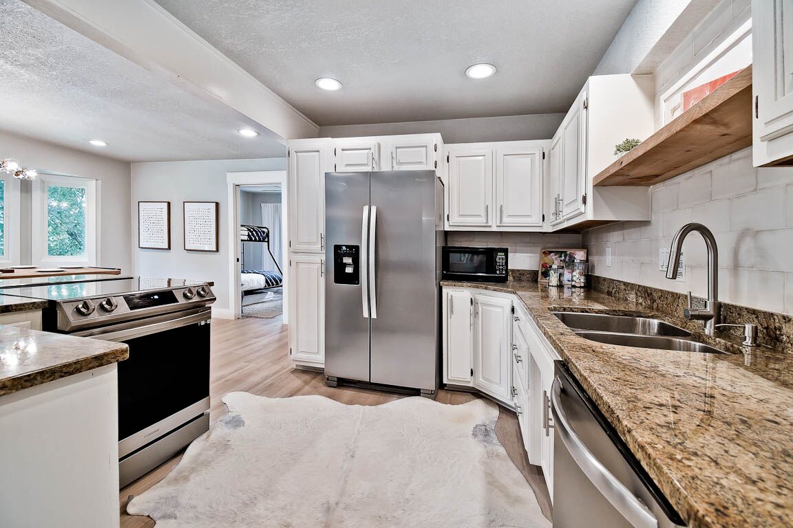 A modern kitchen with white cabinets, stainless steel appliances, granite countertops, and a large refrigerator.