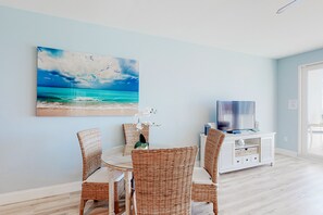 Enjoy meals in this cozy dining area with a round table and four comfortable chairs, accompanied by a beautiful beach scene painting and a flat-screen TV.