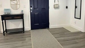 A hallway with a dark blue door, a small table with a mirror and a light fixture, and a patterned rug on the floor. - Close to Disney and the Beaches Full House 3/3 (Orlando)