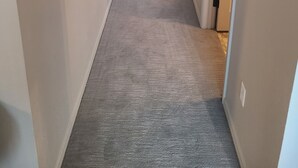 Un pasillo con pisos alfombrados y paredes blancas que conduce a una habitación con una lámpara y una pequeña mesa.