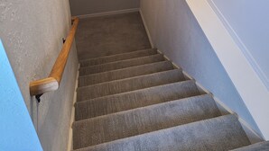 Una escalera con barandilla, peldaños alfombrados y dos cuadros en las paredes.
