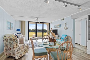 Relax in this inviting living room with a glass-top dining table, wicker chairs, and a plush armchair.