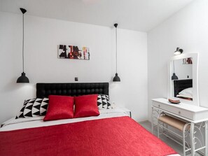 Un dormitorio moderno con un cabecero tapizado negro, una mesita de noche blanca, una manta roja y una almohada con estampado blanco y negro.