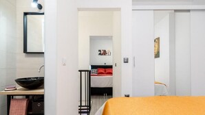 A modern hotel room with a large bed, a bedside table with a black bowl, a small desk with a mirror, and a bathroom with a sink and towel. - Apartment Dionis Domus - Two Bedroom Apartment with Swimming Pool (Vela Luka)