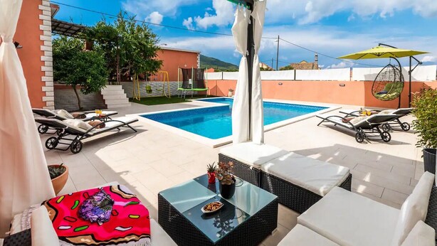 A covered outdoor area with a swimming pool, lounge chairs, and a table with a colorful rug. - Apartment Dionis Domus - Two Bedroom Apartment with Swimming Pool (Vela Luka)