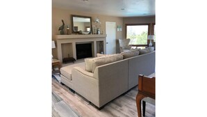 A living room with a beige sofa, a fireplace, and a large window. - Beautiful 3,000 Sq Ft Tropical Oasis (El Cajon)