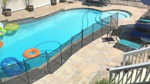 A swimming pool with a stone deck, surrounded by lounge chairs and umbrellas. - Beautiful 3,000 Sq Ft Tropical Oasis (El Cajon)