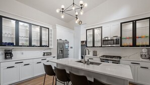 A modern kitchen with white cabinets, a central island with bar stools, stainless steel appliances, and a unique chandelier. - Luxury Retreat in the Mountains! (Thornton)