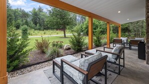 A covered patio with outdoor seating, a view of a golf course, and a stone fireplace. - Luxury Retreat in the Mountains! (Thornton)