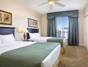 Une chambre d’hôtel avec deux lits, un ventilateur de plafond, une grande fenêtre avec des rideaux et un sol recouvert de moquette.