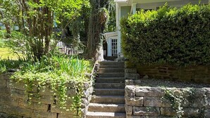 Una escalera de piedra conduce a una casa con porche cubierto, rodeada de abundante vegetación.