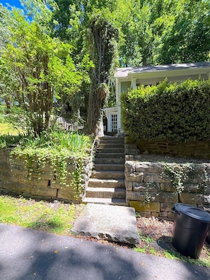 Eine steinerne Treppe führt zu einem Haus mit überdachter Veranda, umgeben von üppiger Vegetation.