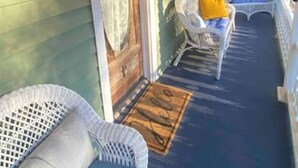Un porche cubierto con una puerta de madera, número 25, y un área de descanso con muebles de mimbre y un cojín azul.