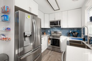A modern kitchen with stainless steel appliances, white cabinets, and a blue-tiled backsplash.