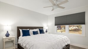 A bedroom with a bed, nightstands, a ceiling fan, a window with blinds, and a view of the outside. - Eudora House with Epic Game Room (Eudora)