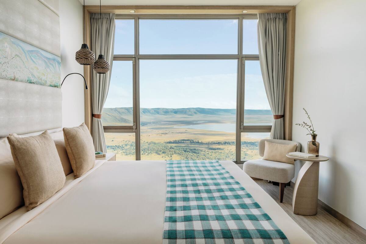 A hotel room with a large bed, a view of the countryside, a chair, and a small table with a vase.
