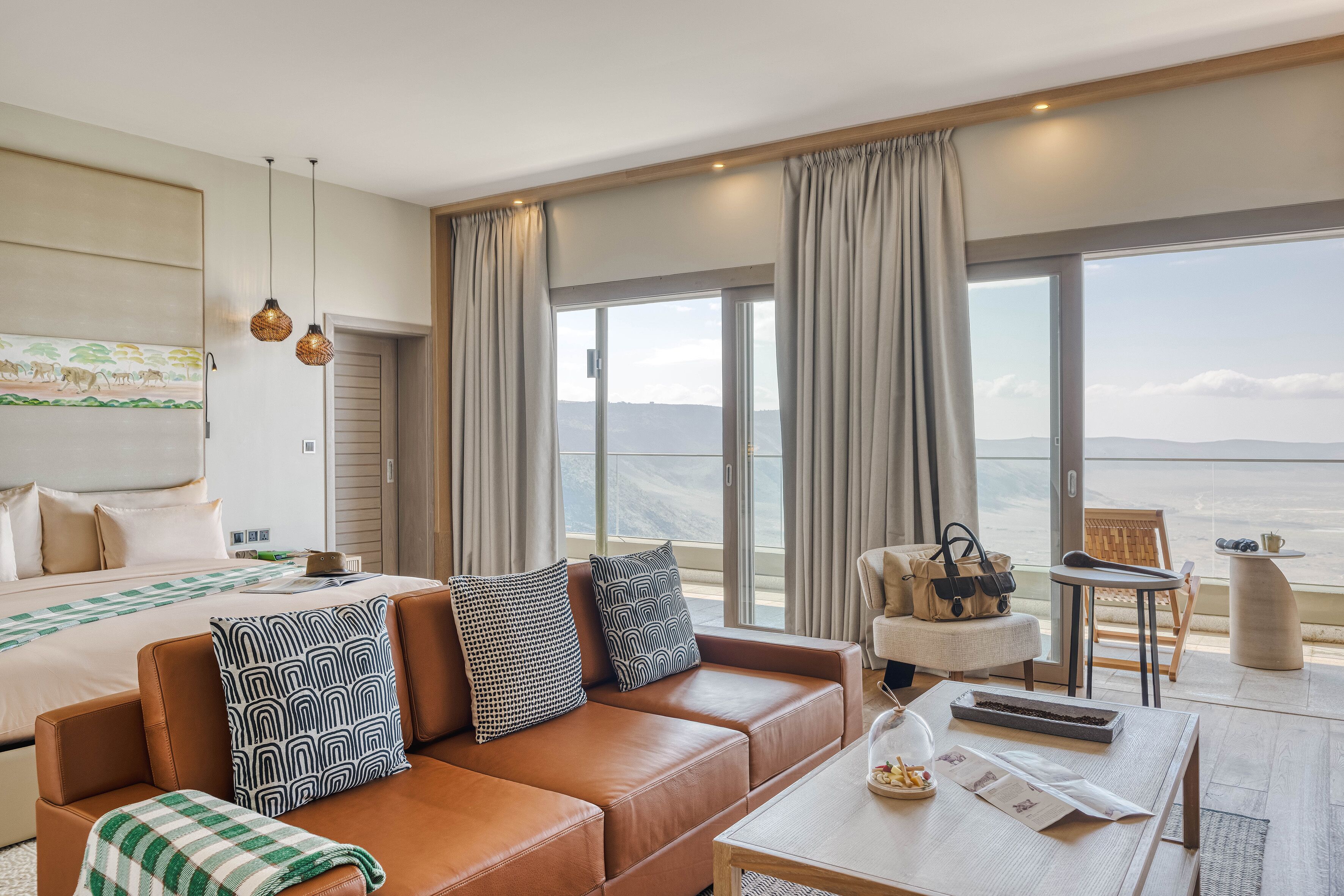Une chambre d’hôtel avec un grand lit, un canapé en cuir marron, une table à manger et une vue sur la mer.