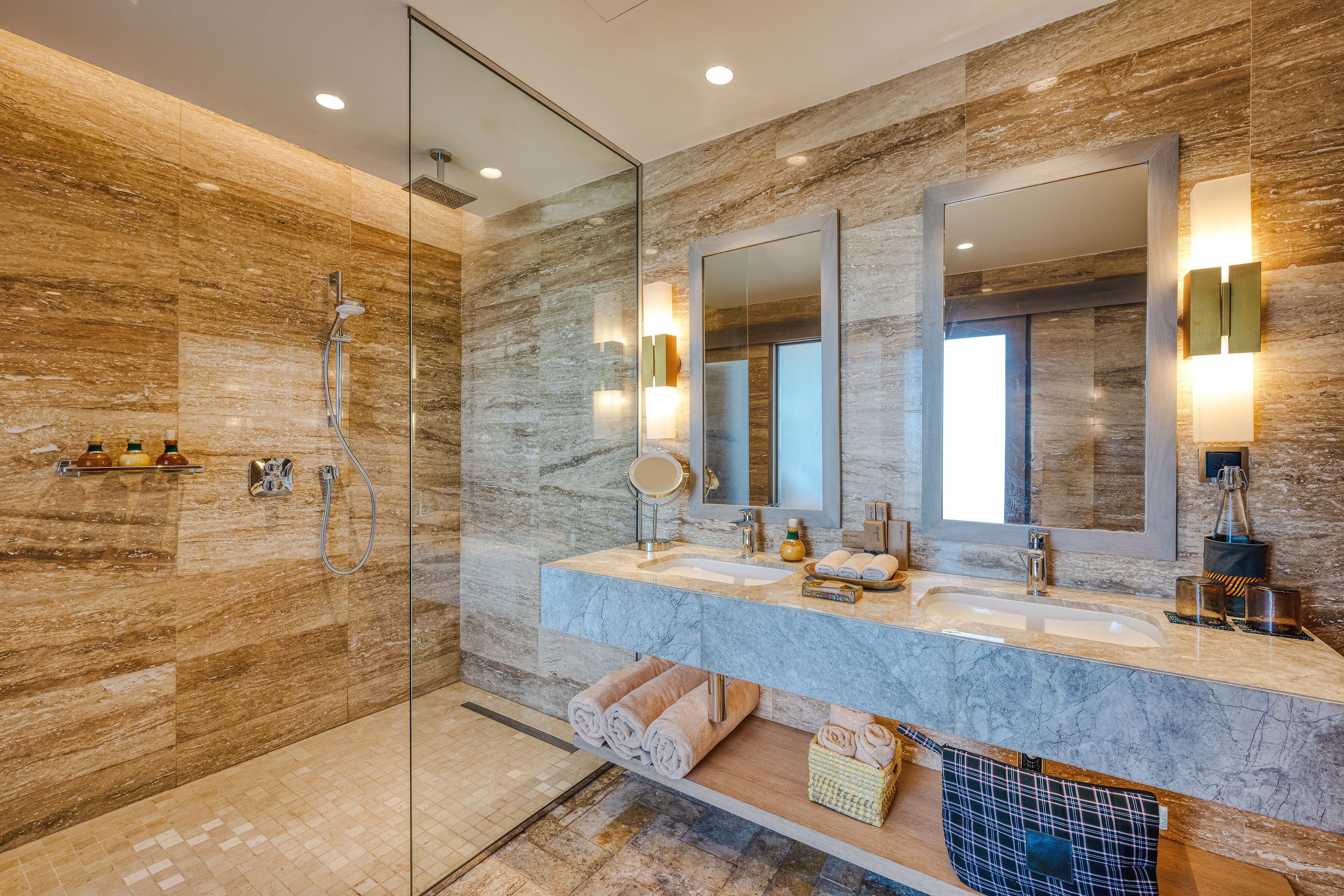 A modern bathroom with a glass-enclosed shower, marble countertops, and multiple mirrors.
