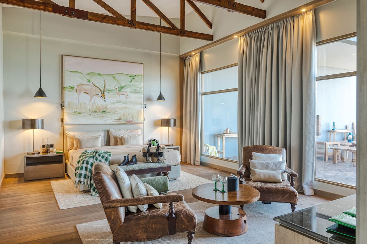 A spacious living room with a large bed, two armchairs, a coffee table, and a painting on the wall.