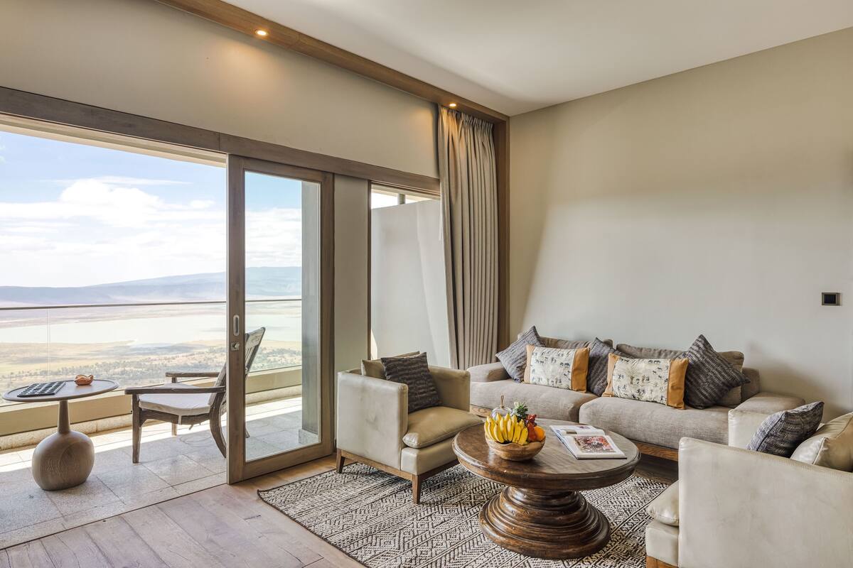 A spacious living room with a sofa, armchairs, a coffee table, and a view of the landscape through large windows.