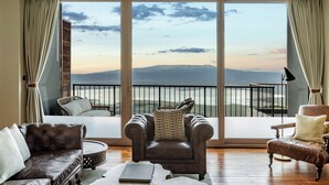 A room with a large sliding glass door leading to a balcony with a view of mountains. There are two leather armchairs and a sofa with cushions. - Ngorongoro Lodge member of Meliá Collection - The Leading Hotels of the World (Ngorongoro)