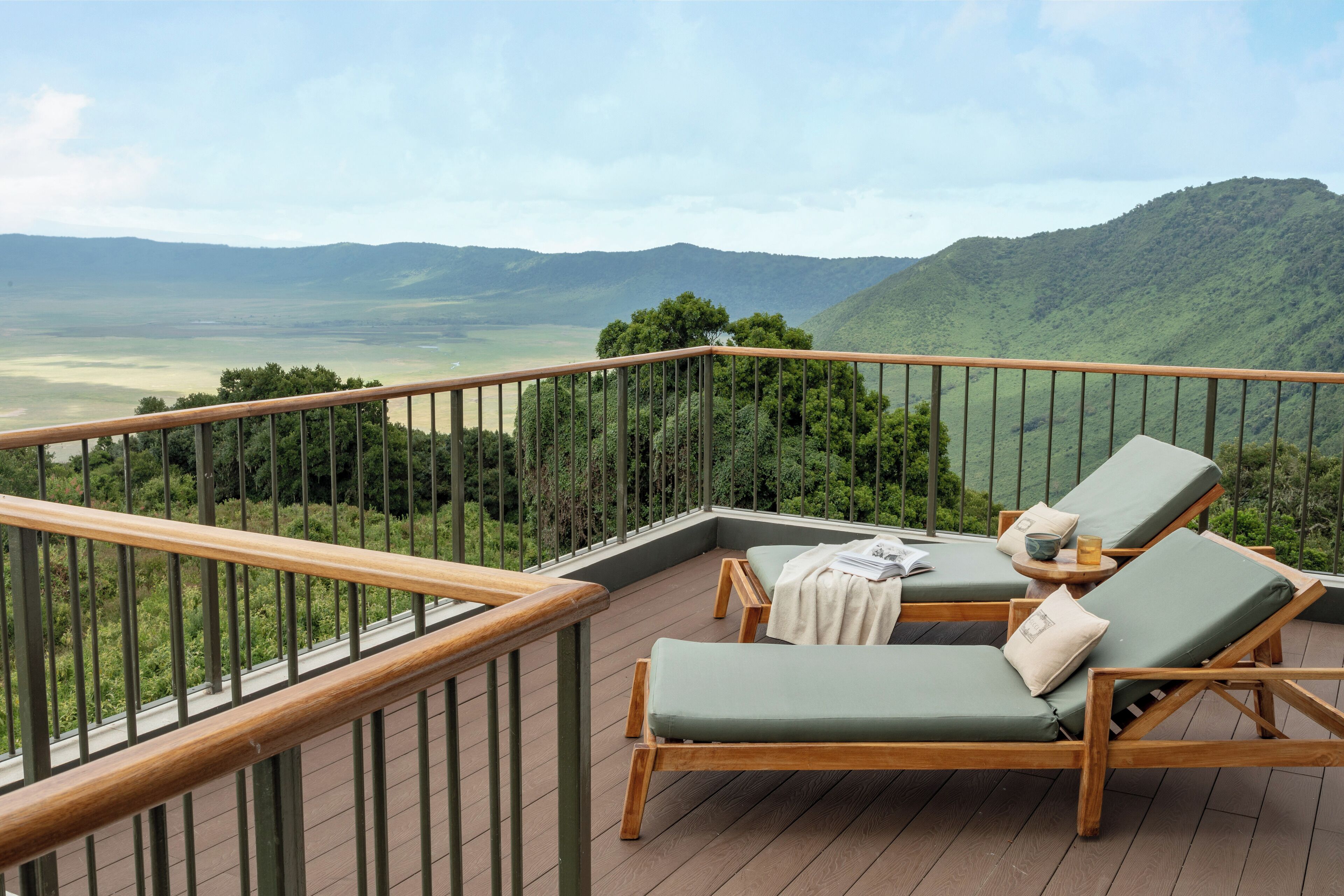 Un balcon avec des balustrades en bois, deux fauteuils avec des coussins et une table sur laquelle se trouvent un bol et un livre.