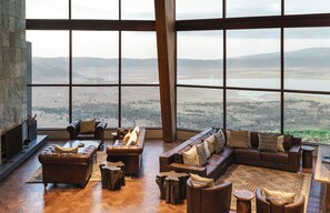 A spacious living area with leather sofas, a fireplace, and large windows offering a view of a valley and mountains. - Ngorongoro Lodge member of Meliá Collection - The Leading Hotels of the World (Ngorongoro)