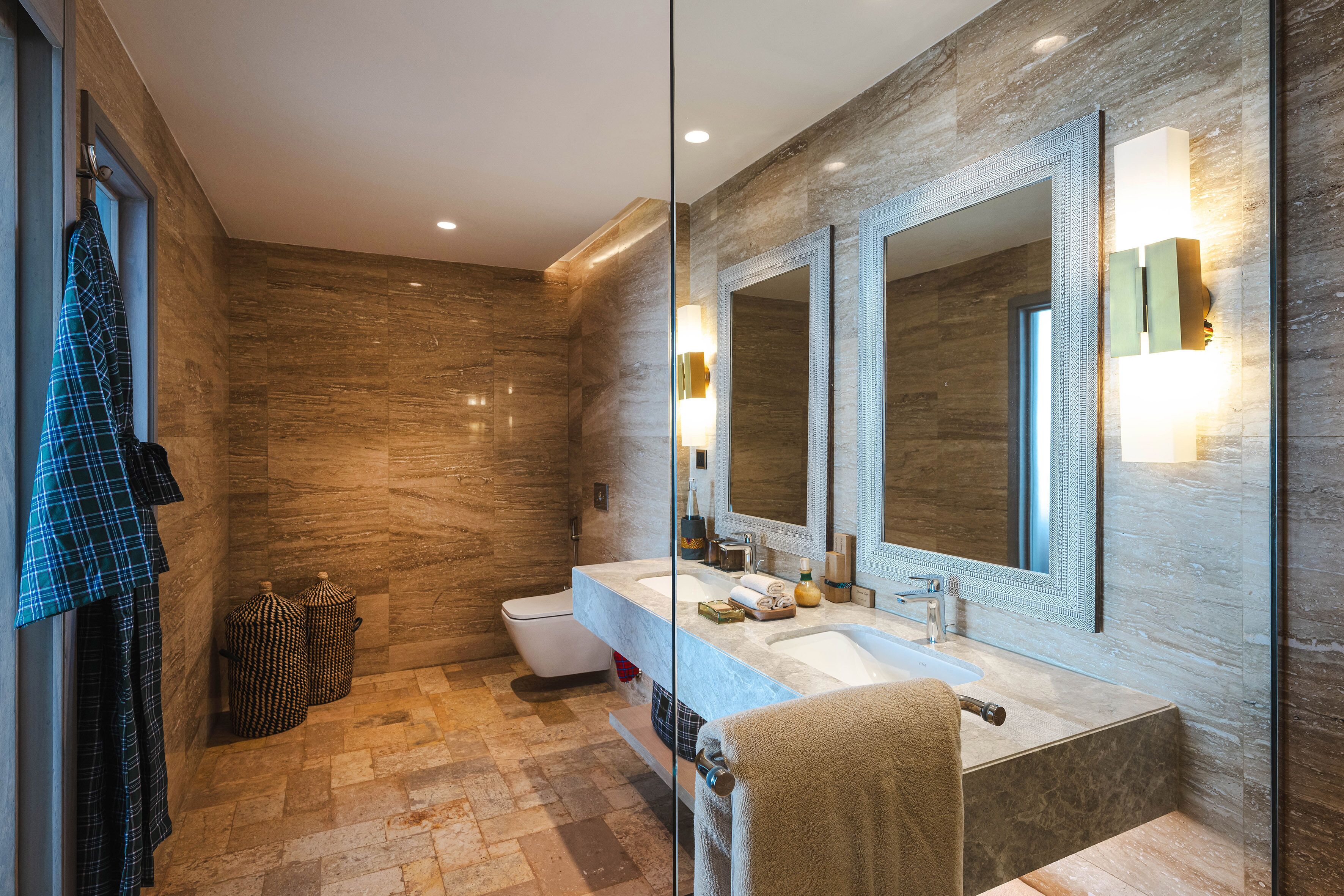 A modern bathroom with a marble wall, a large mirror, a sink, and a toilet.