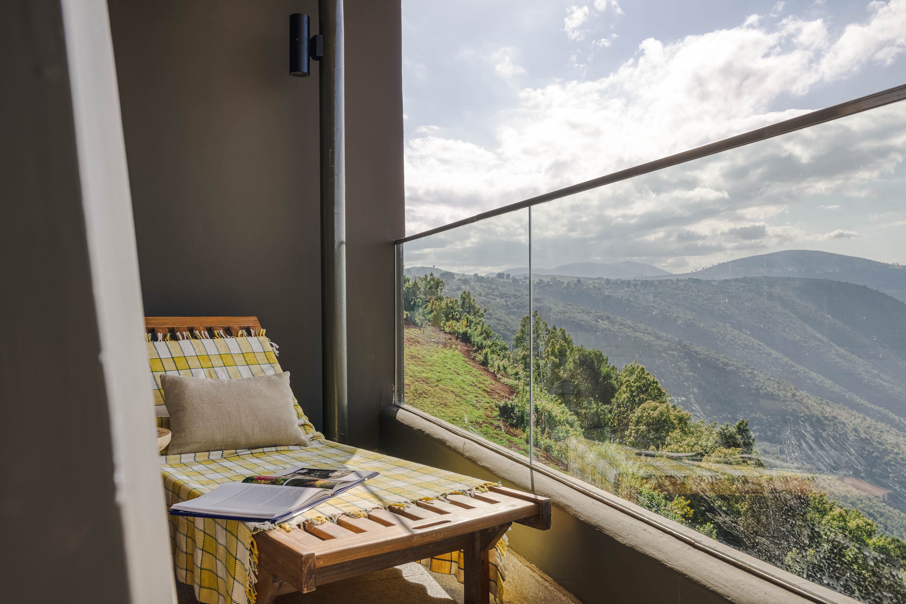 A room with a bed, a wooden table, and a view of a mountainous landscape through a window.