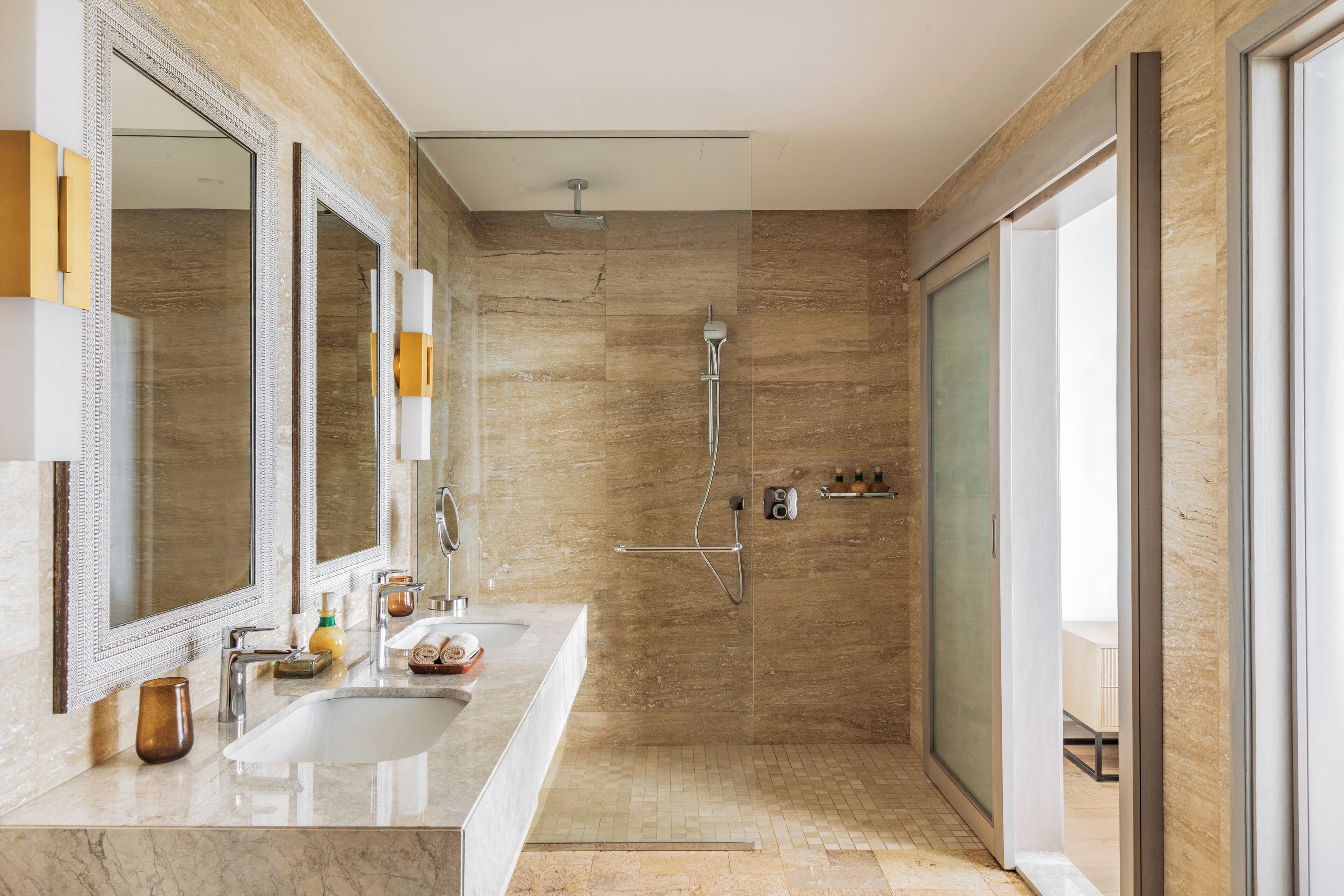 Een moderne badkamer met twee wasbakken, een grote spiegel, een douche en een glazen deur naar een balkon.