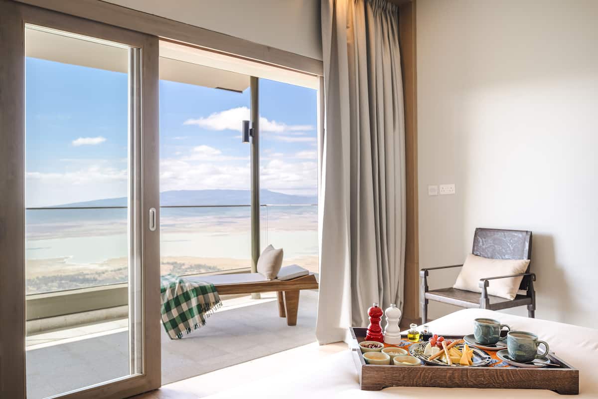 A hotel room with a balcony overlooking a beach, a bed with a tray of breakfast items, and a chair with a cushion.