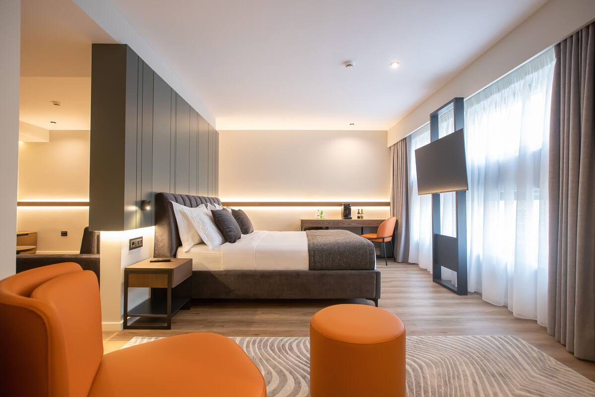 A modern hotel room with a large bed, a desk, a TV, and a view of the city.