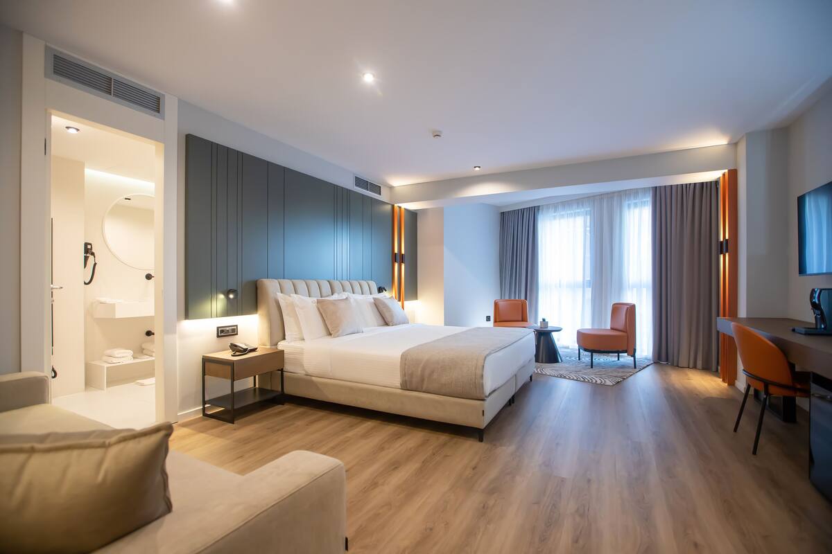 A modern hotel room with a large bed, a desk, and a seating area.