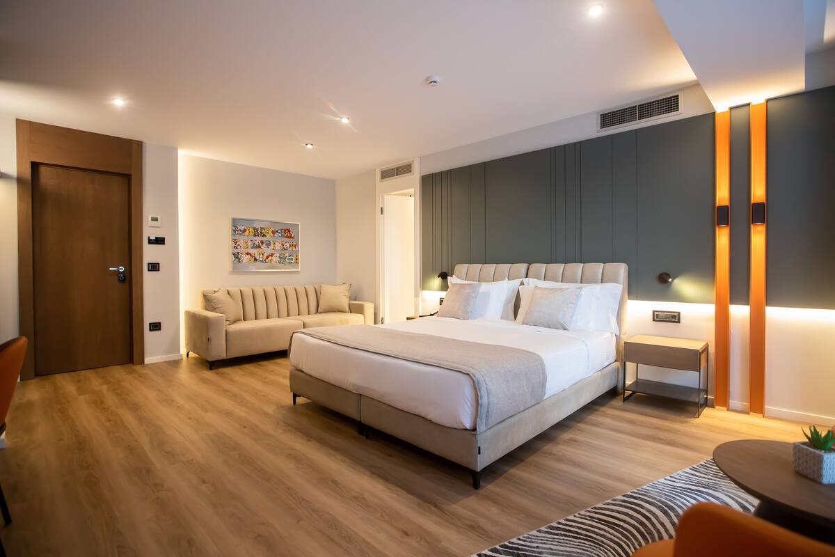 A modern bedroom with a large bed, a sofa, a bedside table, and a small table with a plant.