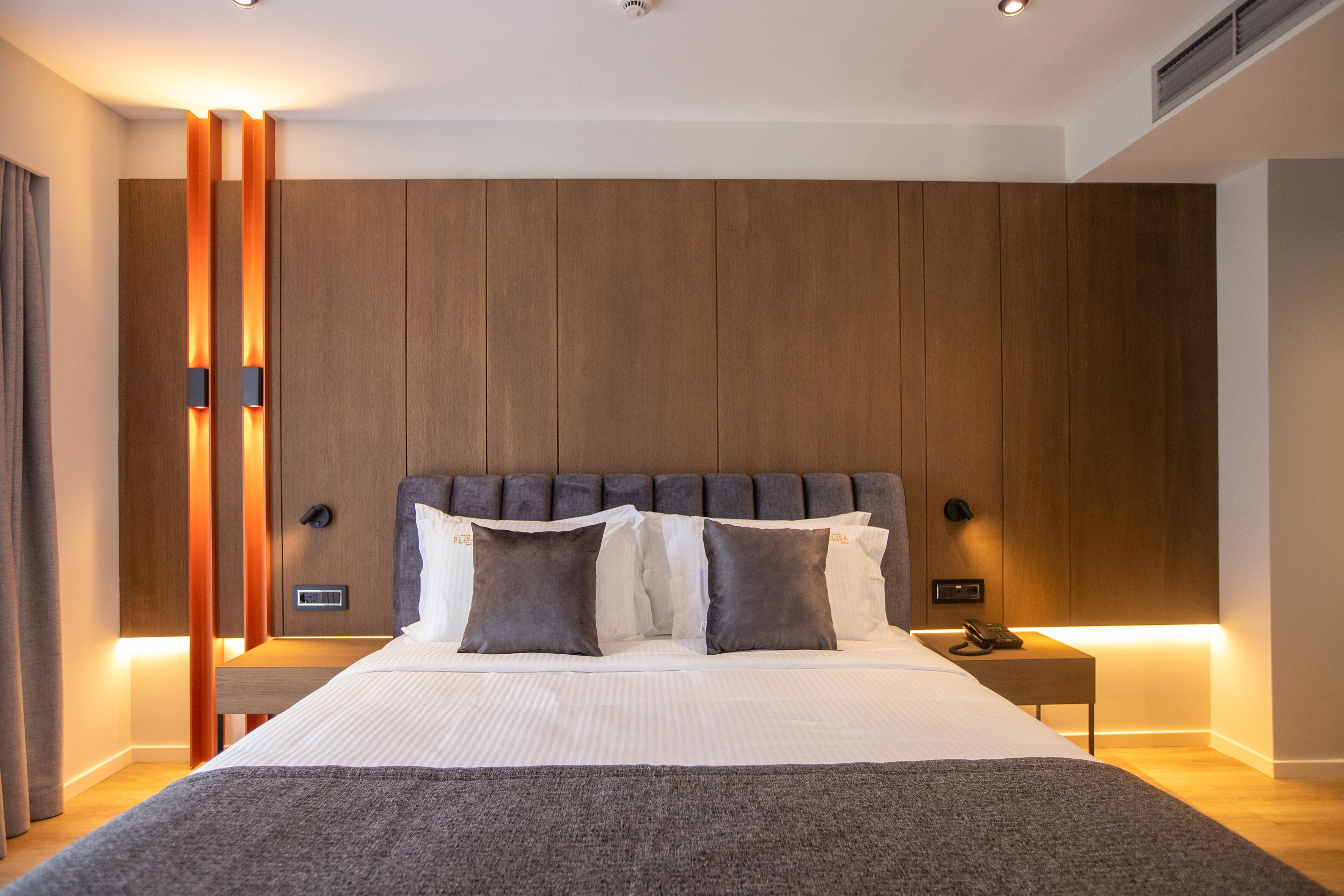 A modern hotel room with a large bed, wooden paneling on the walls, and a bedside table with a phone.