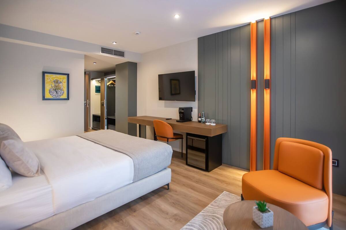A modern hotel room with a bed, desk, chair, TV, and a small table with a plant.