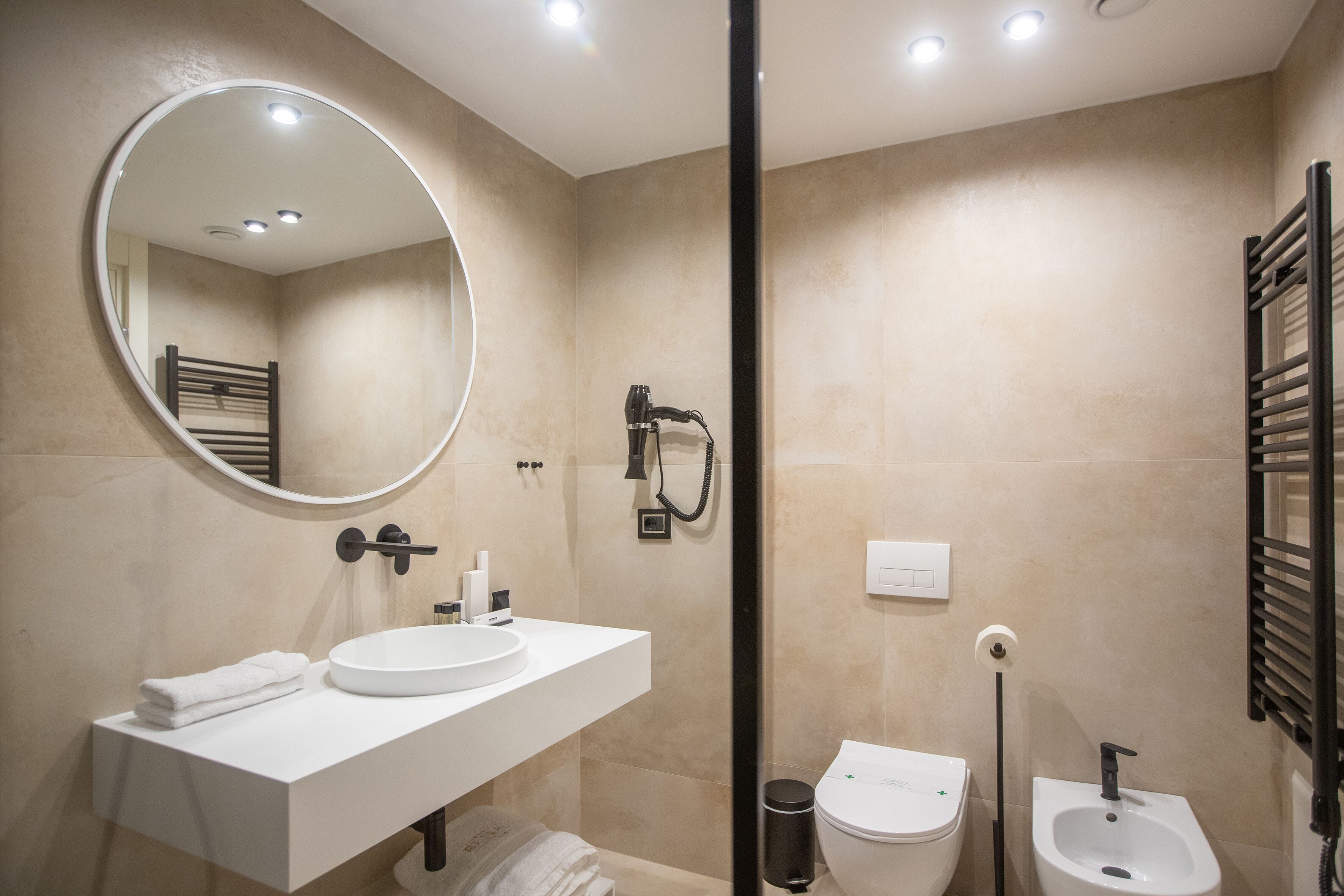 Een moderne badkamer met een ronde spiegel, een wit wastafelmeubel, een toilet en een bidet.