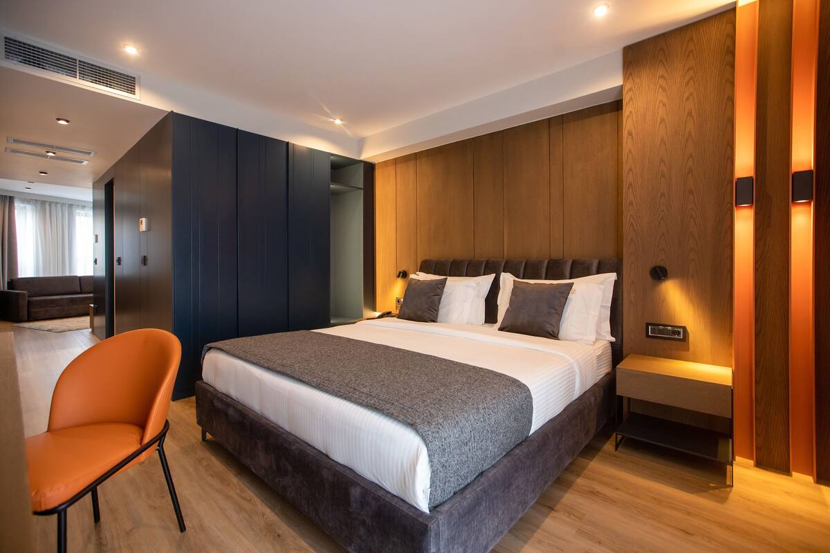 A modern hotel room with a large bed, a wooden headboard, a bedside table, and a chair.