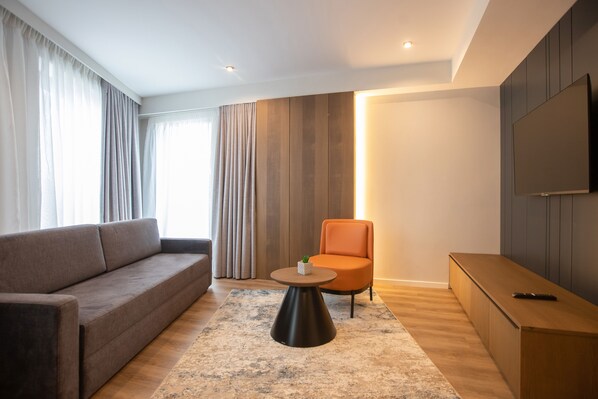 Una sala moderna con un sofá, un sillón naranja, una mesa de centro redonda y un televisor en la pared.
