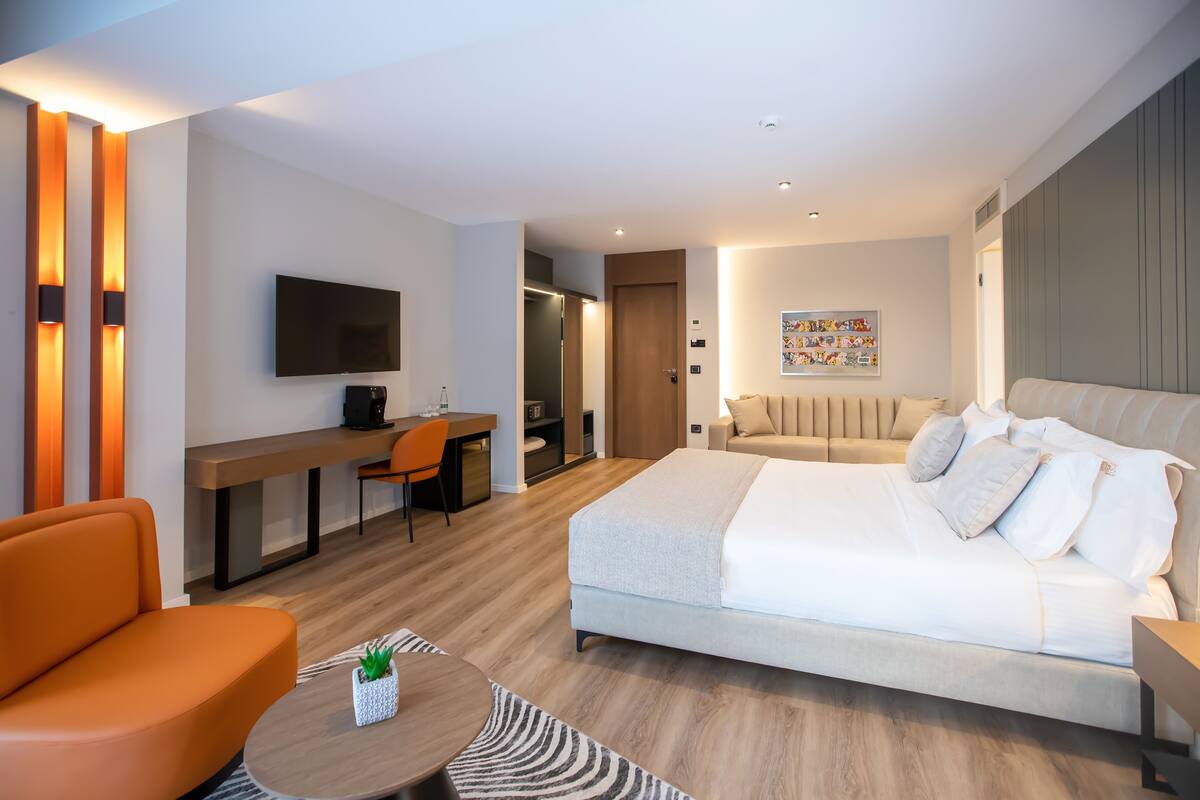 A modern hotel room with a large bed, a desk, a TV, and a sofa.