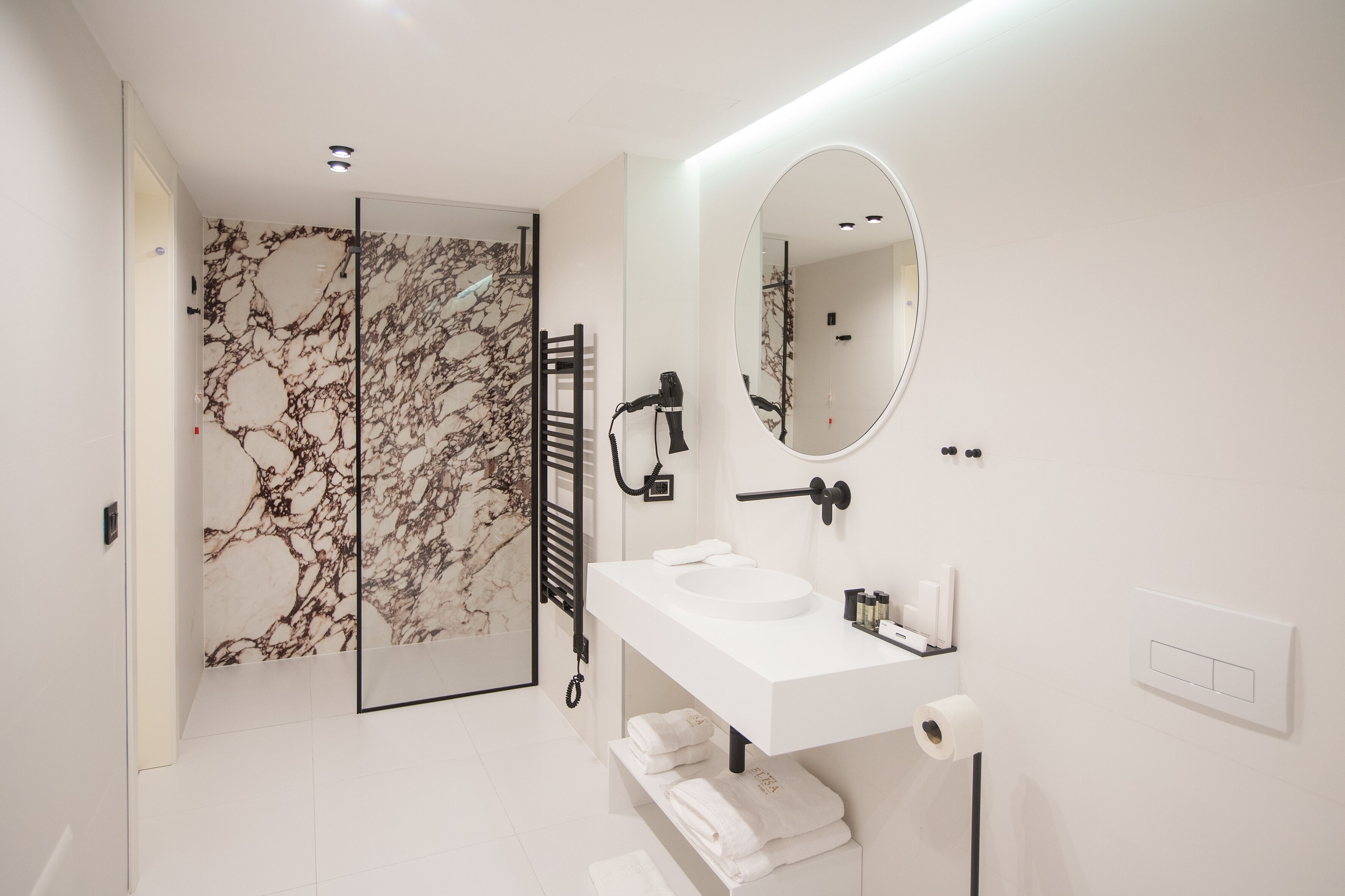 A modern bathroom with a marble shower wall, a white sink with a mirror, and neatly folded towels.