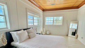 A spacious bedroom with a large bed, wooden ceiling, and multiple windows providing natural light. - Bimini Vacation Apartment - APT#3 (Bimini)