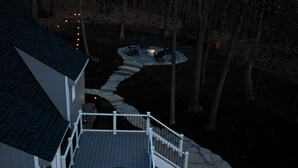 A two-story house with a deck, a stone pathway, and a fire pit area. - A-Frame Mountain Retreat (Gerrardstown)